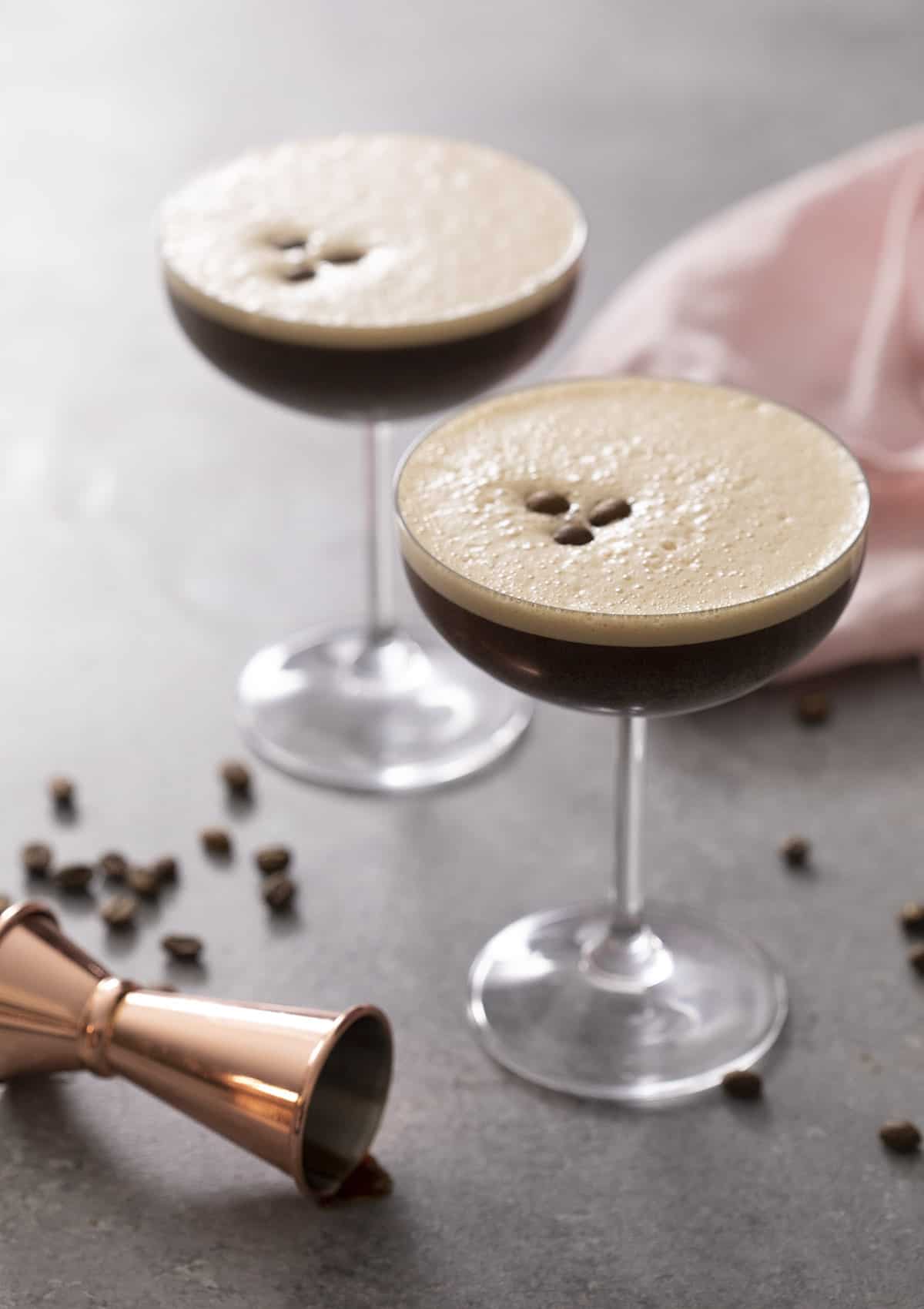 An Espresso martini on a gray surface with coffee beans scattered around