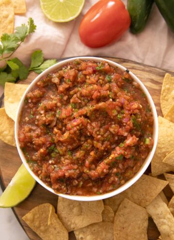 A close up of salsa in a bowl with tortilla chips around it
