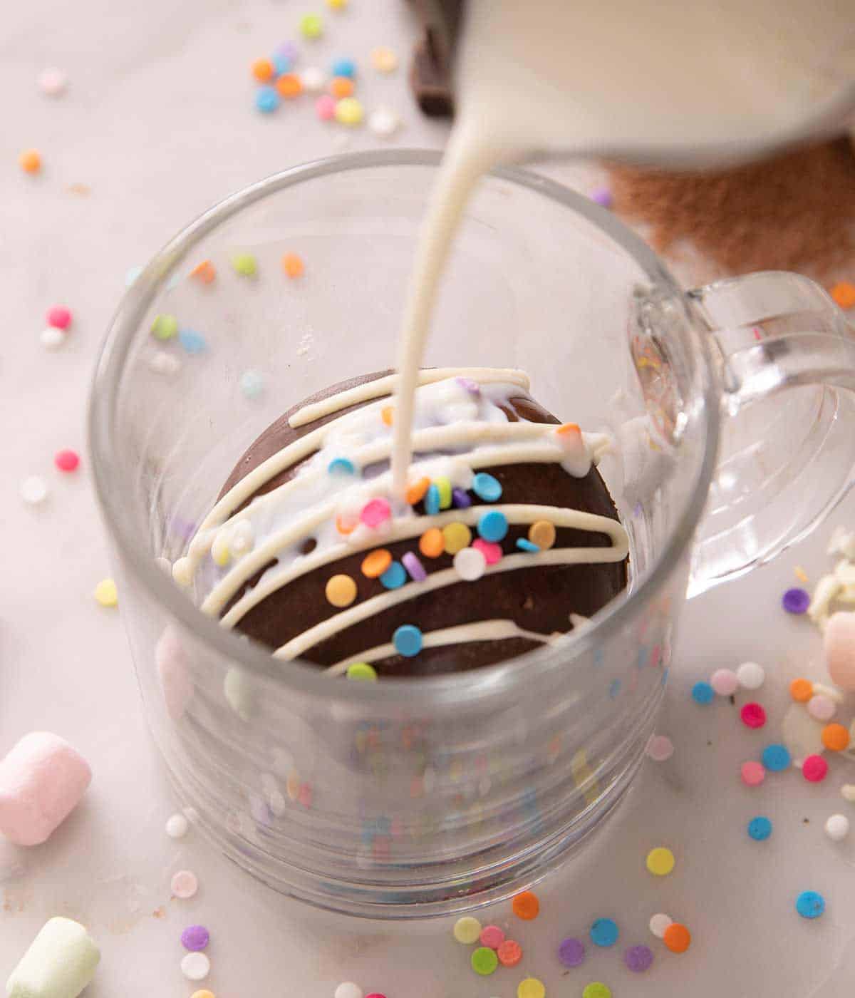 Milk getting poured on top of a hot chocolate bomb in a glass