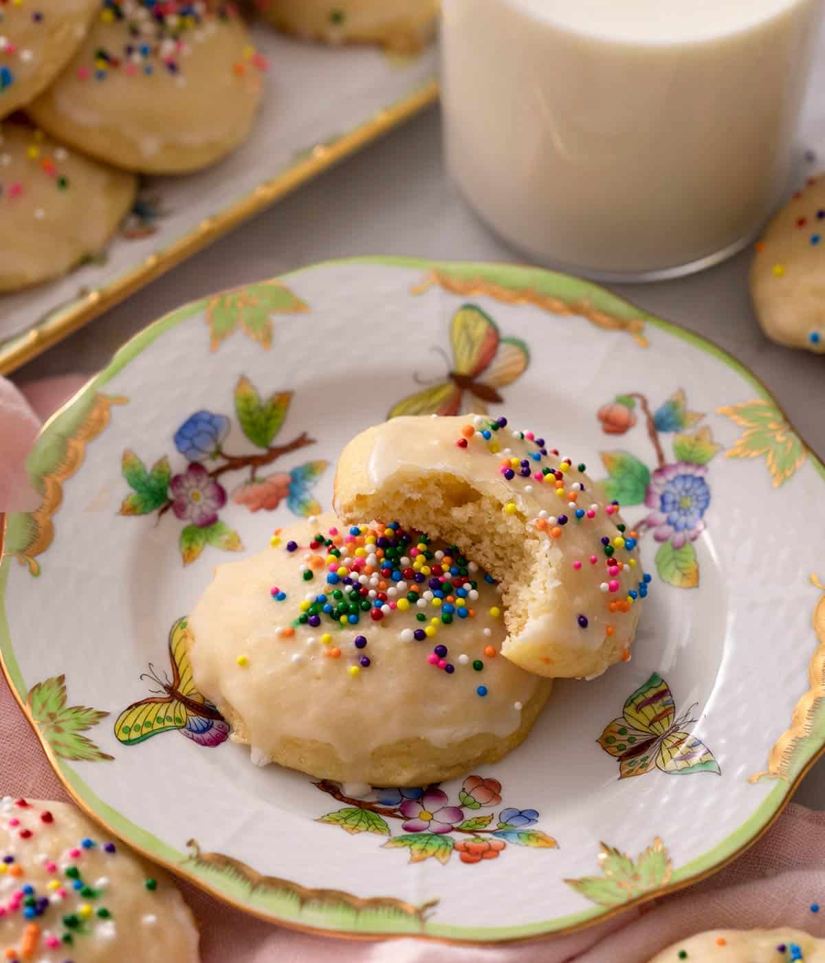 Two ricotta cookies on a china plate one with a bite out