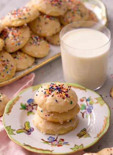 Ricotta cookies stacked on top of each other with a glass of milk in the background