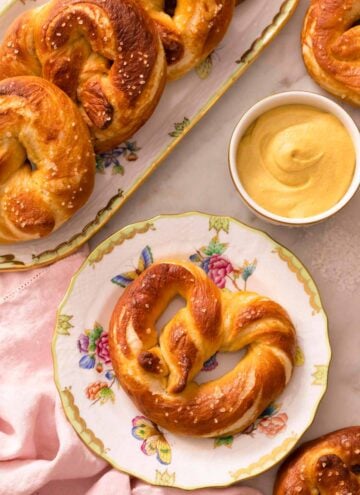 An overhead shot of a soft pretzel on a plate next to mustard