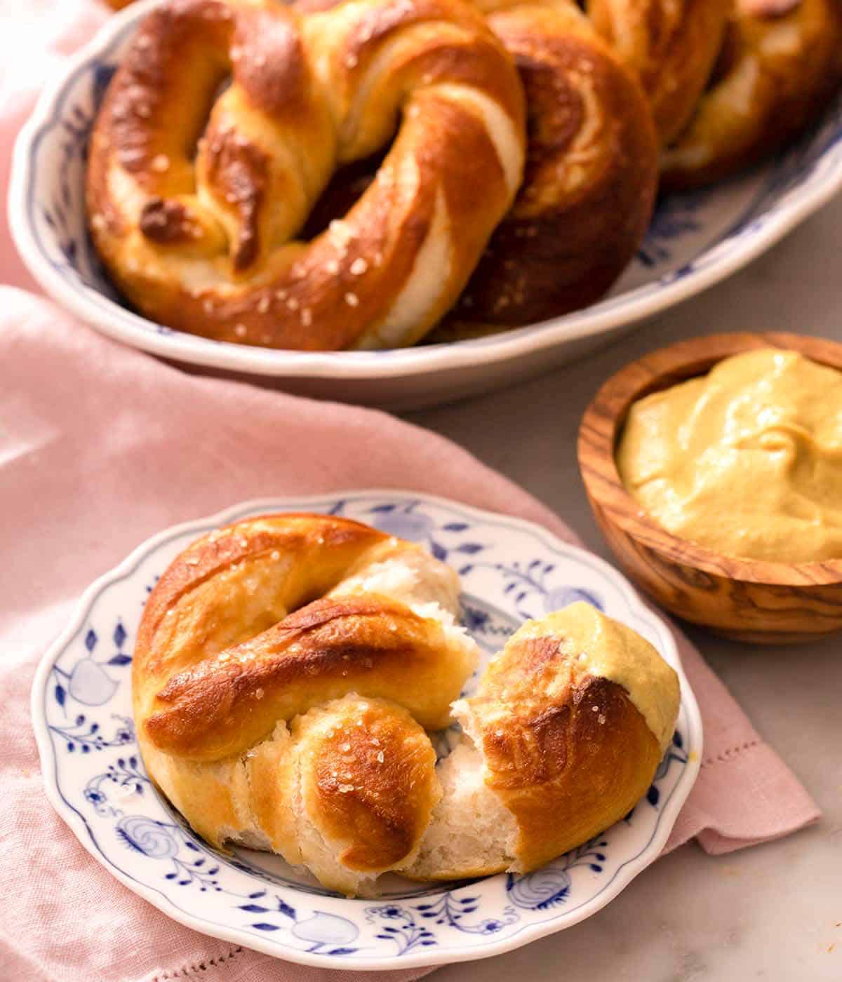 A close up of a soft pretzel on a blue plate with mustard in the background