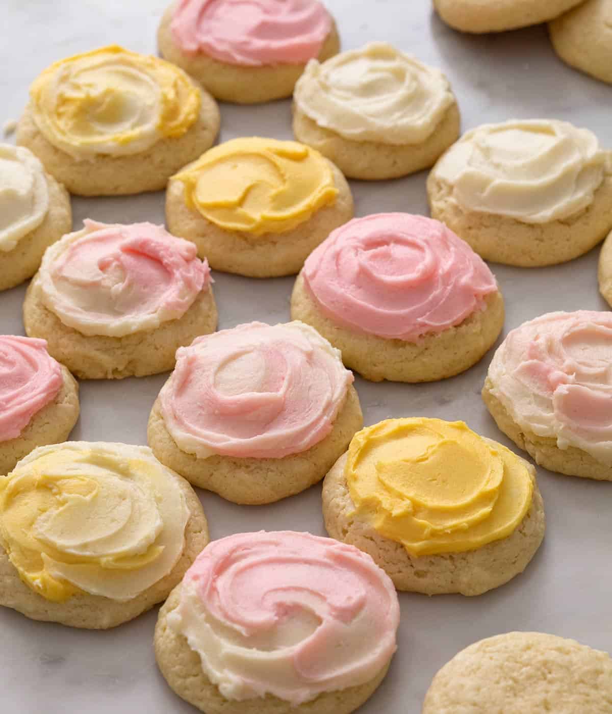 Sour cream cookies with pink and yellow frosting on a white work surface