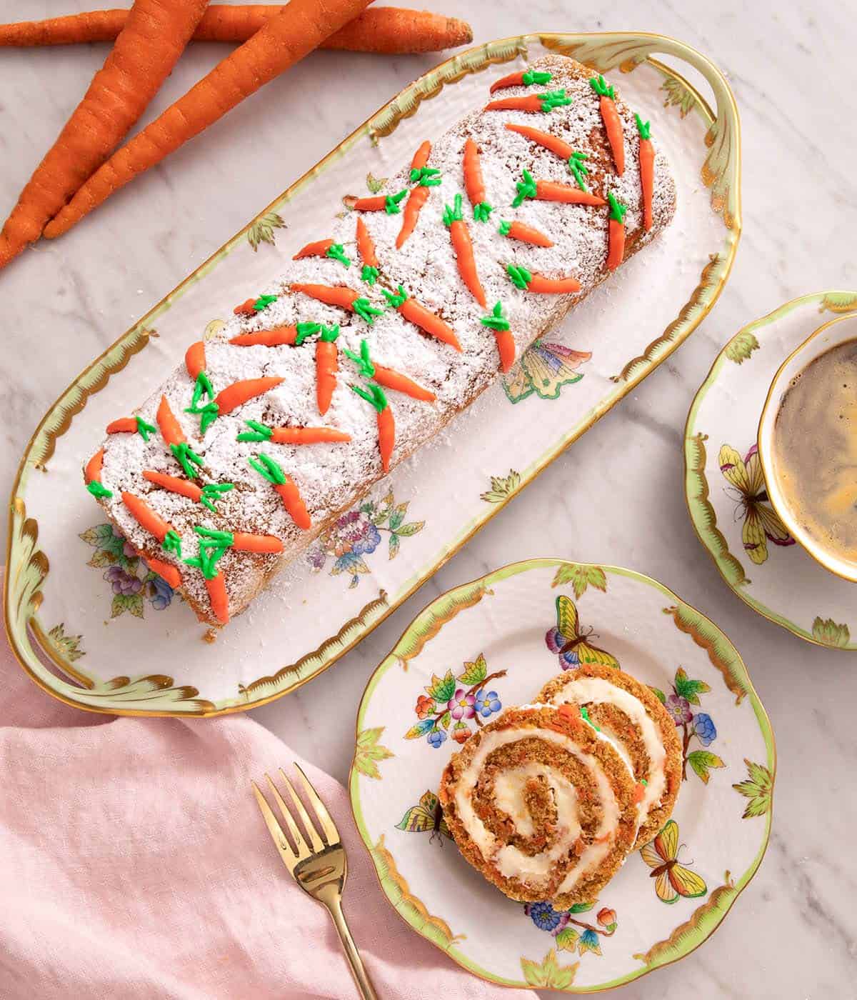 An overhead shot of a carrot cake roll on a serving plate and two slices cut 