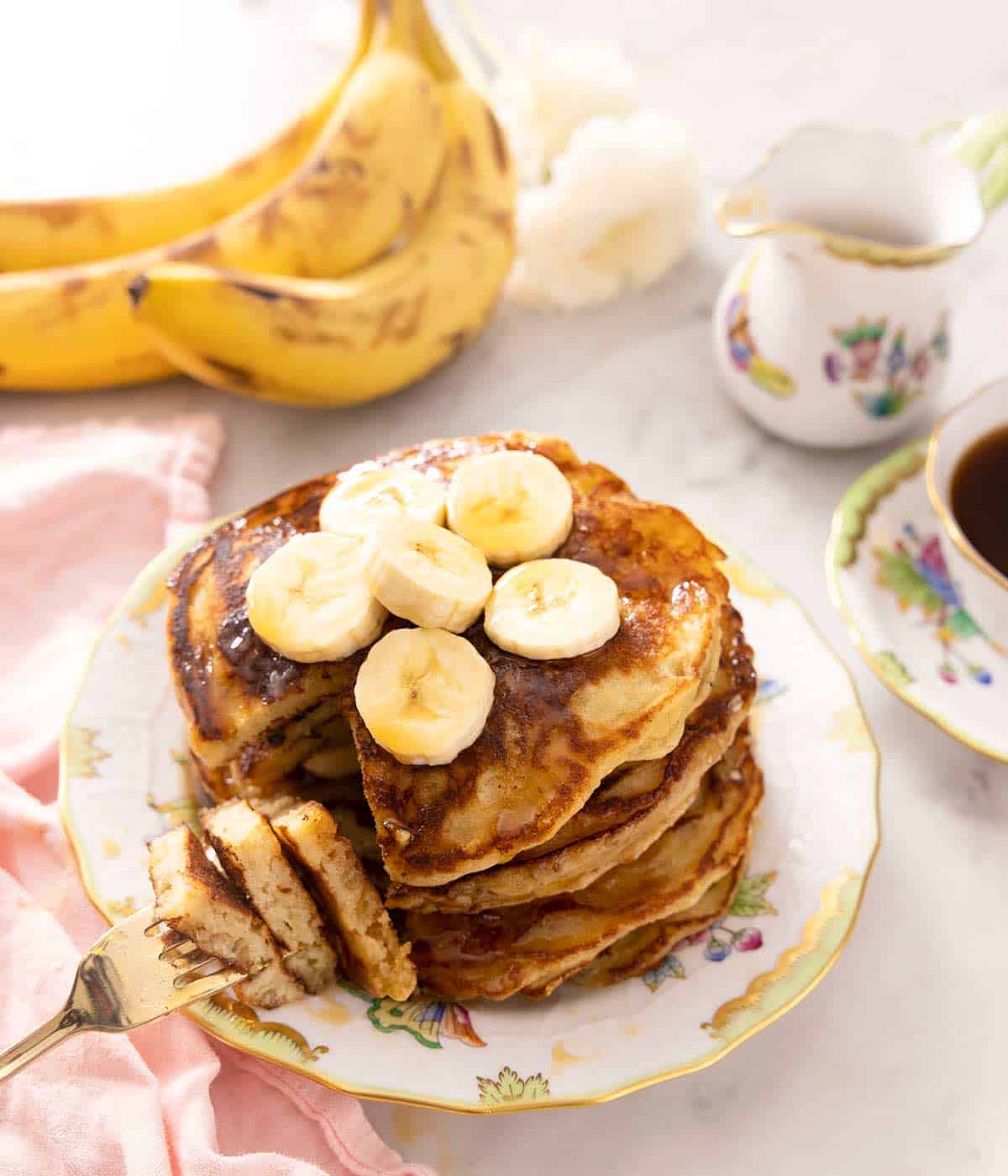 A stack of banana pancakes on a plate and some of a fork