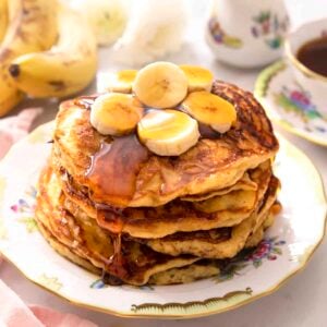 A stack of banana stacks with sliced bananas and maple syrup on top.