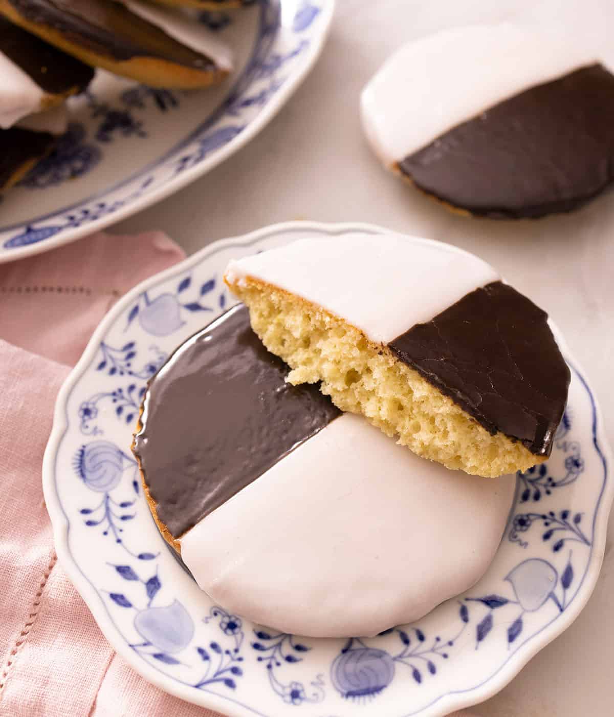 A plate of black and white cookies with one cut in half, stacked over another.