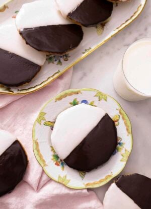 Overhead view of multiple black and white cookies with one in a plate next to a glass of milk.