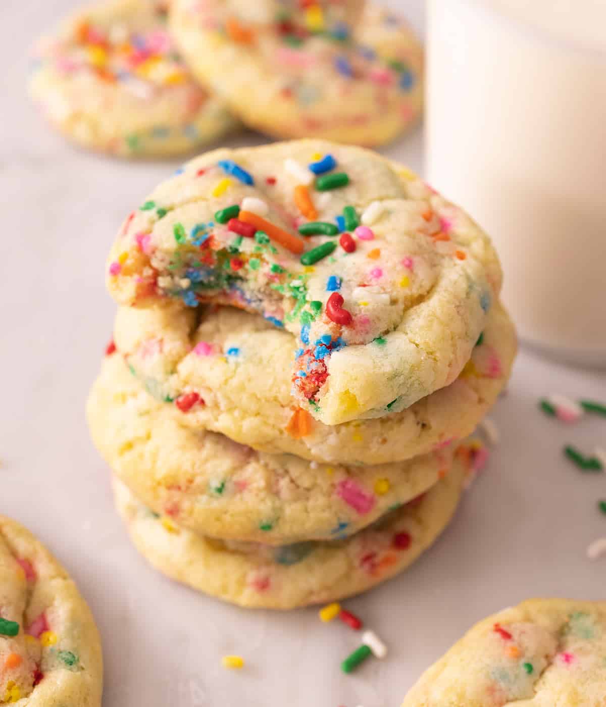 A stack of four funfetti cookies with a bite taken out of the top cookie.