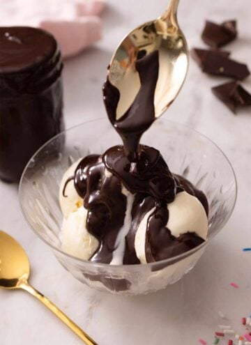 Hot fudge being spooned over top of ice cream in a bowl.