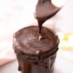 A glass jar of hot fudge with a spoon scooping some out.