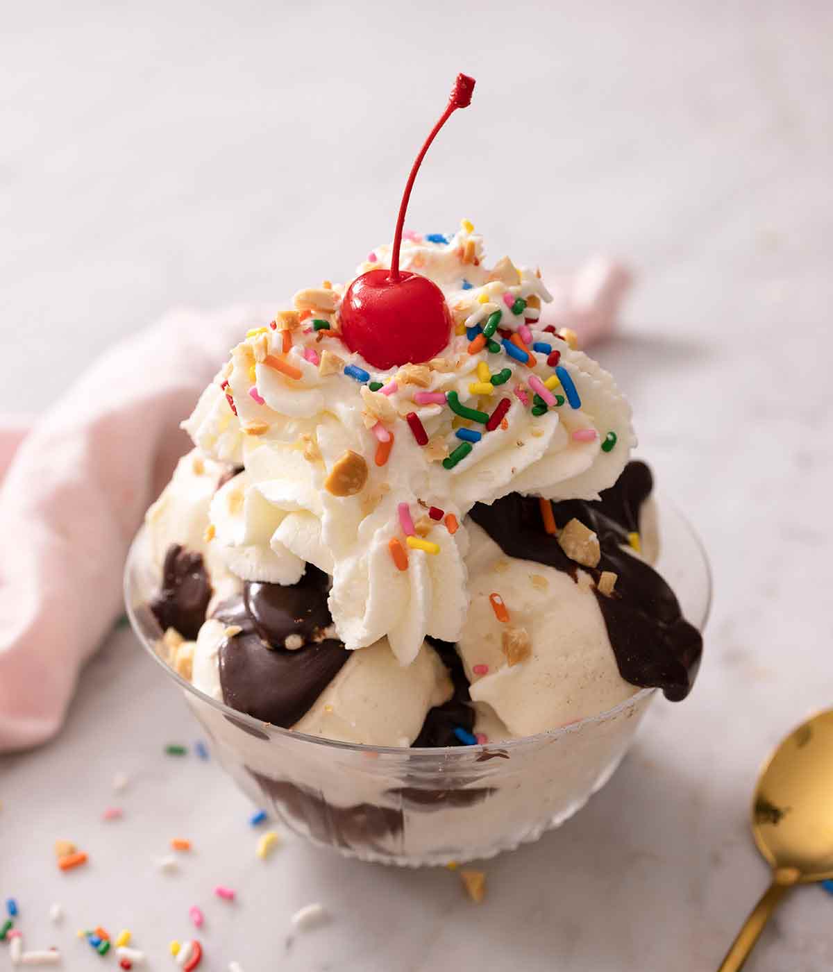 A hot fudge sundae in a glass bowl topped with whipped cream, sprinkles, nuts, and a cherry.