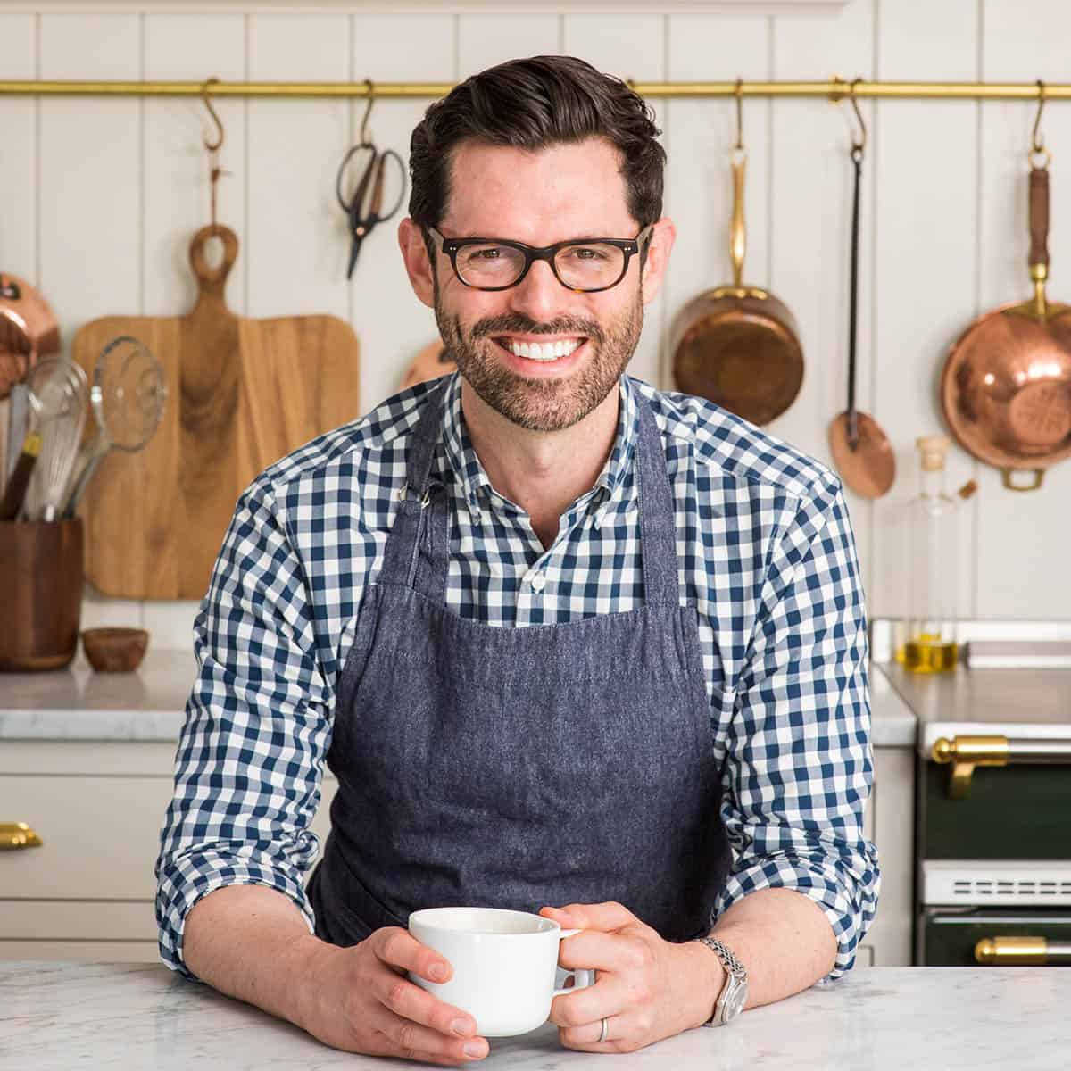 Photo of John Kanell holding a coffee cup in the kitchen.