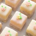 Overhead view of rows of petit fours with little yellow and pink roses on top.