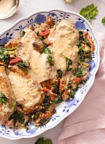 A white and blue floral platter with Tuscan chicken breasts with the sauce over top.