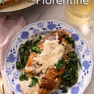 Pinterest graphic of a blue and white floral plate of a serving of chicken florentine beside a glass of wine.