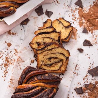 Pinterest graphic of an overhead view of a loaf of sliced babka with chopped chocolate and cocoa powder dusted around it and a second loaf in the pan off to the side.