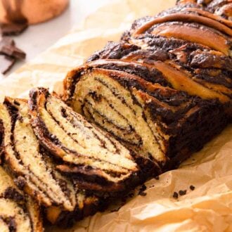 A babka loaf on brown parchment paper with three slices cut beside the loaf, showing the chocolate swirls inside the loaf.