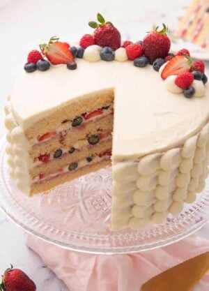 A Chantilly cake with a slice cut out showing the four tiers with berries in between.