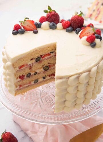 A Chantilly cake with a slice cut out showing the four tiers with berries in between.