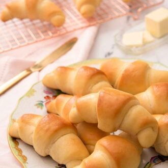 A plate of multiple crescent rolls with a cooling rack with more rolls in the background.