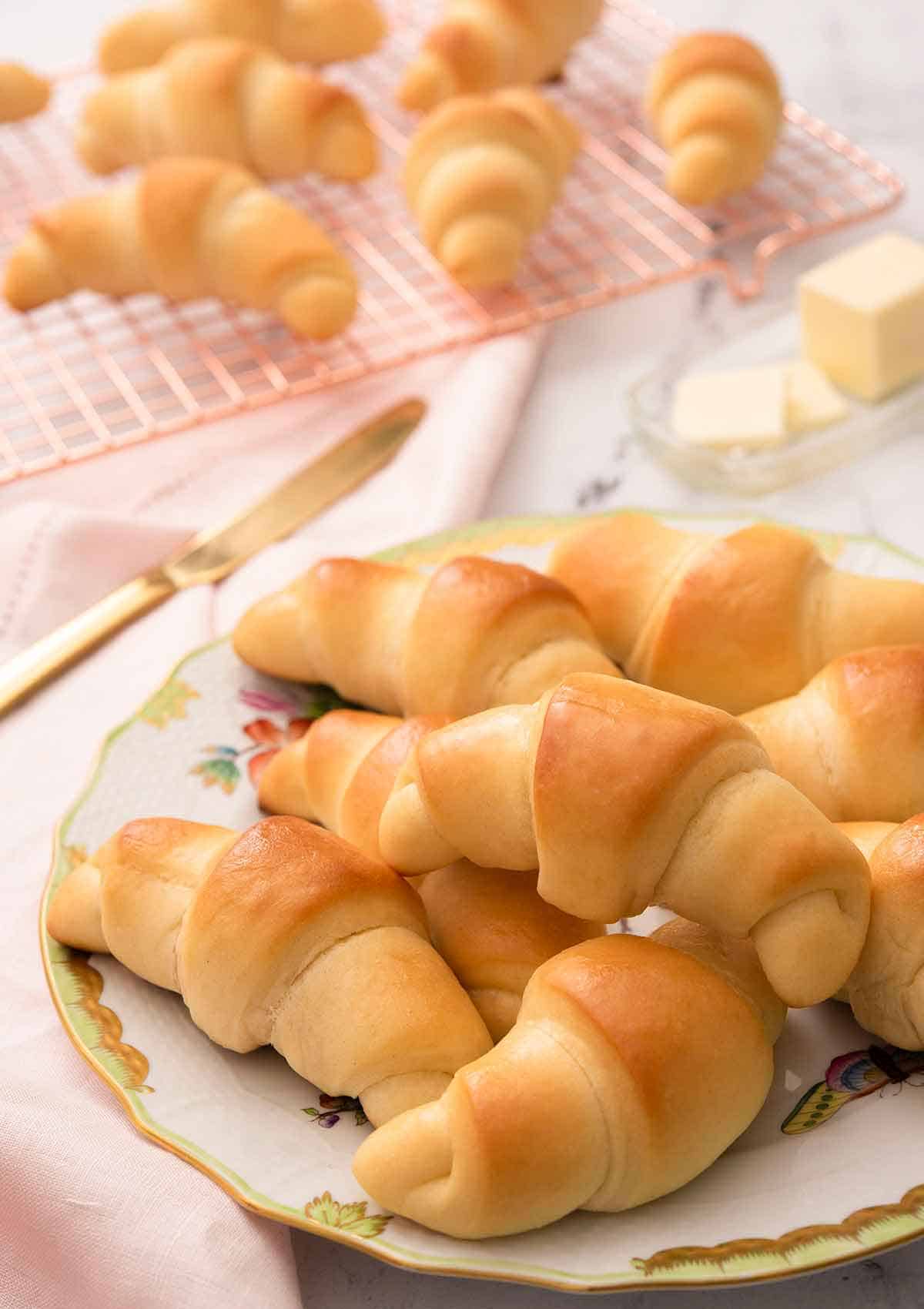 A plate of multiple crescent rolls with a cooling rack with more rolls in the background.