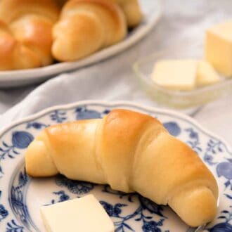 Pinterest graphic of a crescent roll on a blue and white plate with a slice of butter.