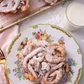 Pinterest graphic of an overhead view of a funnel cake with powdered sugar on a plate with a glass of milk beside it.