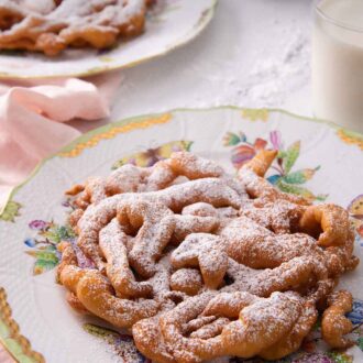 Pinterest graphic of two plates, one in front, each with a funnel cake on it with a dusting of powdered sugar on top.
