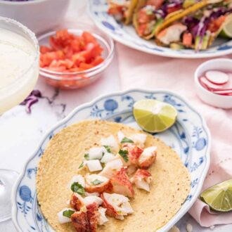 Pinterest graphic of an oval plate with a tortilla with lobster meat in the middle with the toppings in bowls around it.
