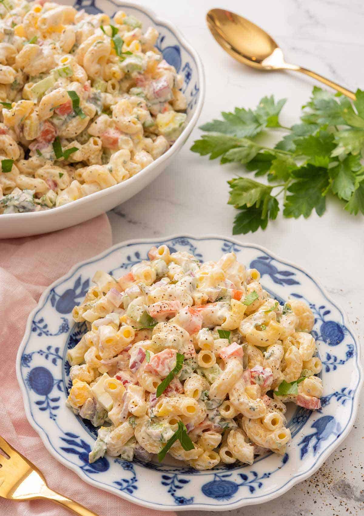 A plate of macaroni salad in front of a bowl on a marble surface.