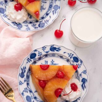 Pinterest graphic of the overhead view of two plates, each with a slice of pineapple upside down cake on them with a dollop of whipped cream.