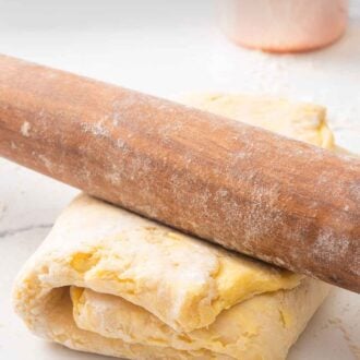 Pinterest graphic of a wooden rolling pin overtop of folded puff pastry on a floured surface.