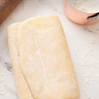 Pinterest graphic of a folded piece of puff pastry beside a cup of flour and a rolling pin.