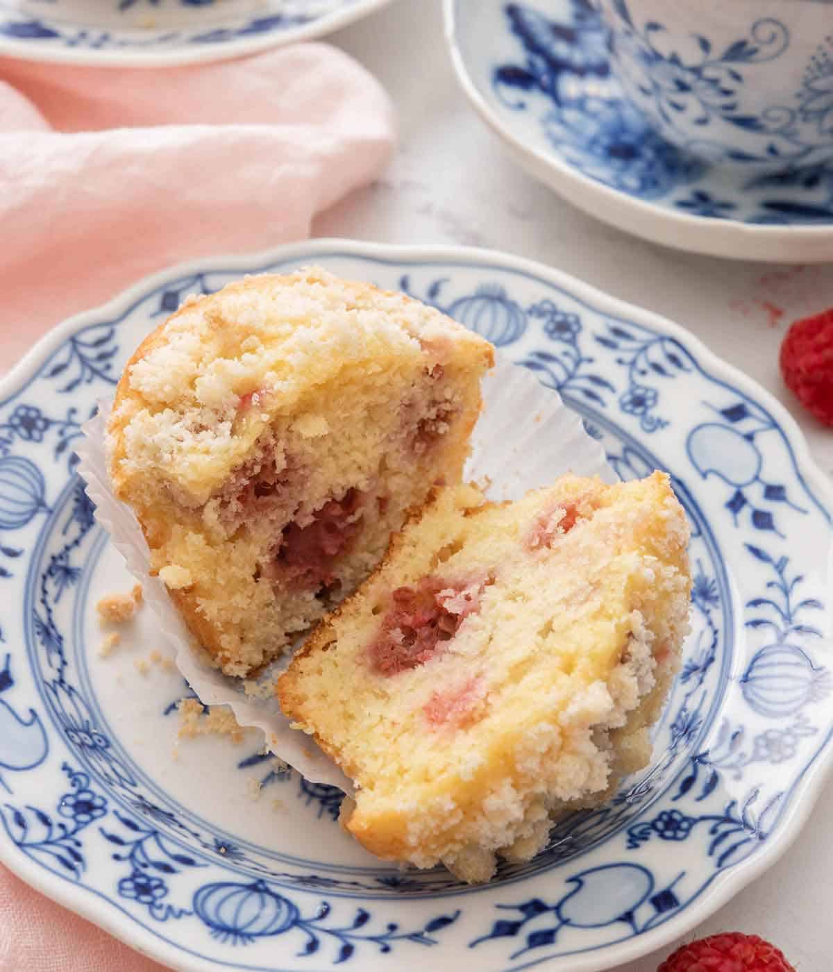 A raspberry muffin cut in half in the muffin liner on a blue and white plate.