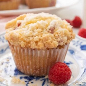 A close profile view of a raspberry muffin with a raspberry in front of it.