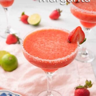 Pinterest graphic of a strawberry margarita in a glass with a salted rim with a halved strawberry as garnish. Strawberries and cut limes scattered around the background.