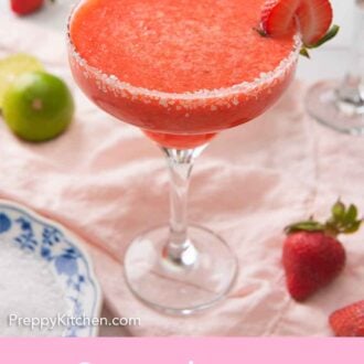 Pinterest graphic of a strawberry margarita with a halved strawberry on the rim, on top of a pink napkin with ingredients around it.