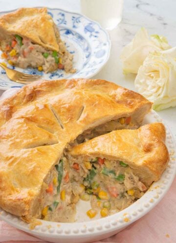 A turkey pot pie, cut opened with a slice removed and placed on a plate behind it.