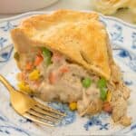 Close up of a serving of turkey pot pie on a blue and white plate and a fork beside it.