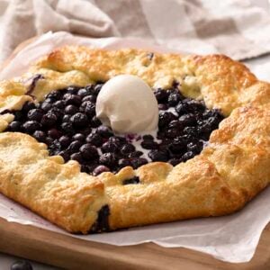 A blueberry galette topped with a scoop of vanilla ice cream on a cutting board.