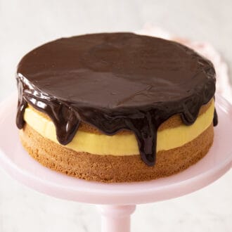 A Boston Cream Pie with silky chocolate ganache on a pink cake stand.