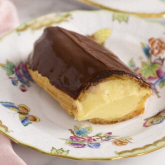 An eclair filled with vanilla pastry cream on a porcelain plate.