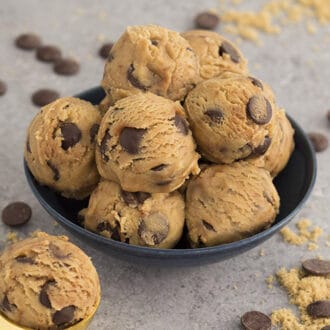 A blue bowl filled with scoops of edible cookie dough dotted with chocolate chips.
