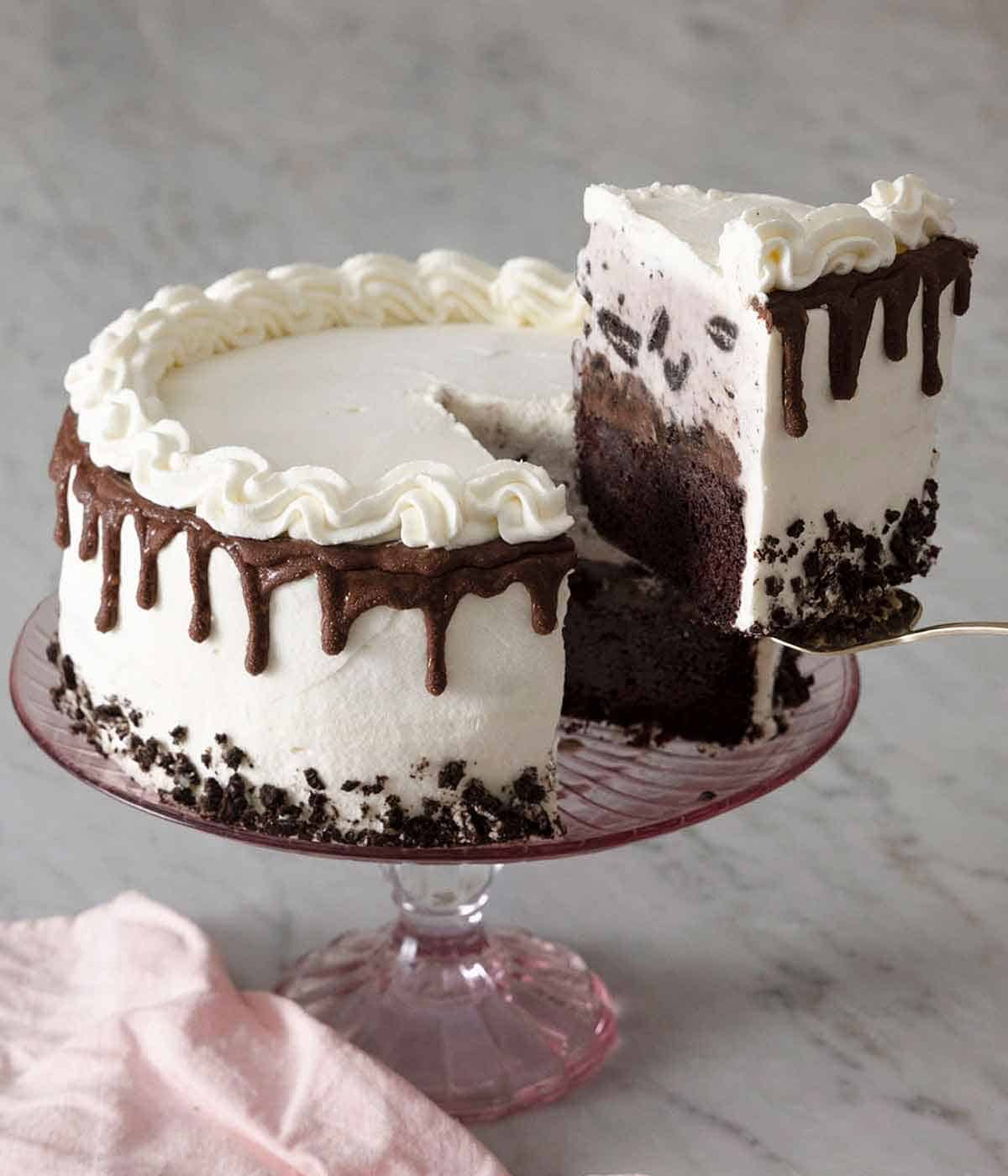 An ice cream cake on a cake stand with a slice being lifted up with a cake serving spatula.