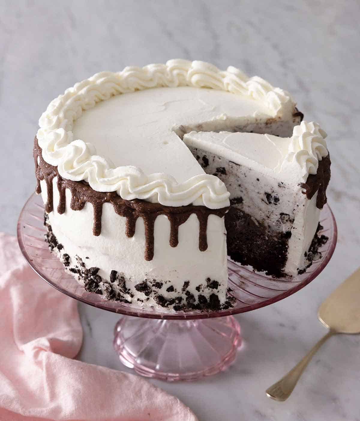 A pink cake stand with an ice cream cake with a slice cut out and another cut but still on the cake stand.