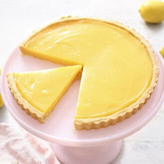 A lemon tart on a pink cake stand with two pieces removed.