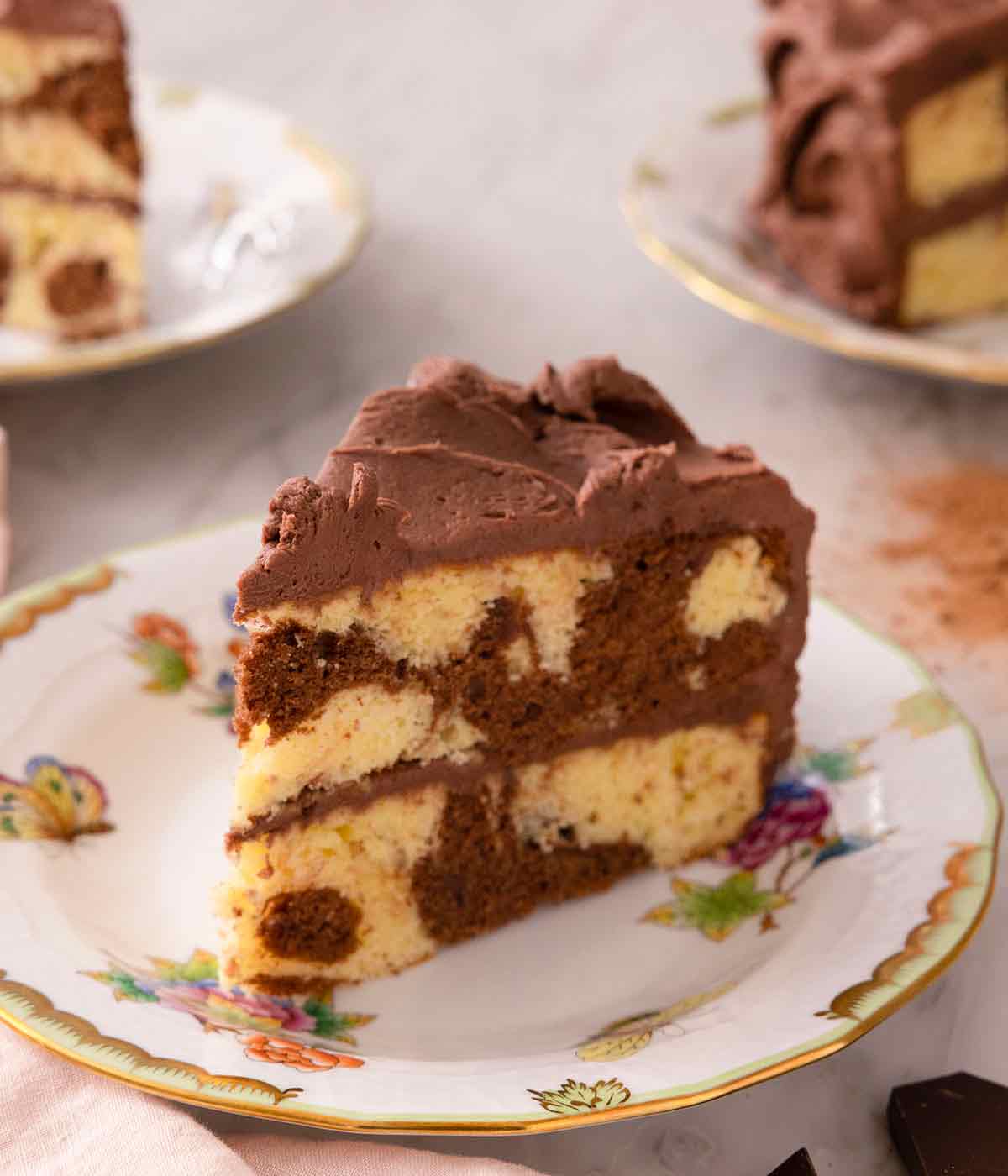 A slice of two tiered marble cake with chocolate buttercream frosting on a plate.