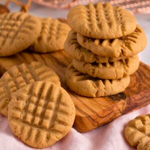 A group of peanut butter cookies stacked on a small wooden board.